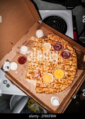 Nach einer wilden Party in einem chaotischen Haus wurde eine alte, halbgefressene Pizza hinterlassen, die im Stil eines Blitzes vor der Kamera gedreht wurde. Stockfoto