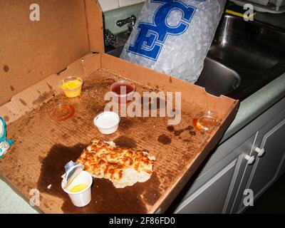 Nach einer wilden Party in einem chaotischen Haus wurde eine alte, halbgefressene Pizza hinterlassen, die im Stil eines Blitzes vor der Kamera gedreht wurde. Stockfoto