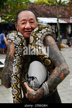 Ein tätowierte balinesischer Mann mit seiner Python um seinen Körper gewickelt. Stockfoto