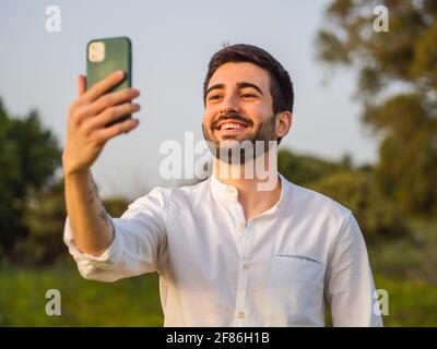 Glücklicher, gutaussehender Spanier, der ein Selfie im Park macht Stockfoto