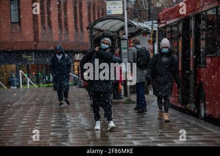 London, Großbritannien. 12 2021. April: Pendler machen sich durch einen Schneesturm auf, als sie am ersten Tag aus dem Bus zur Arbeit in Wimbledon aussteigen.in England werden die Einschränkungen des Coronavirus aufgehoben, damit Menschen ihre Frisur machen und außerhalb von Pubs und Restaurants essen und trinken können. 12. April 2021 Wimbledon, England. Kredit: Jeff Gilbert/Alamy Live Nachrichten Stockfoto