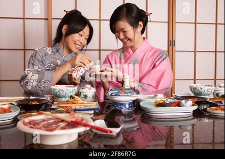 Glückliche junge japanische Frauen in Kimonos trinken Tee zum Mittagessen Stockfoto