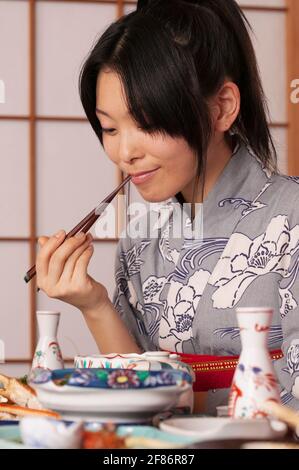 Junge Frau im Kimono, die traditionelle japanische Mahlzeit mit Essstäbchen isst Stockfoto