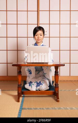 Junge Frau im Kimono, die am Laptop an der Shoji-Tür arbeitet Stockfoto