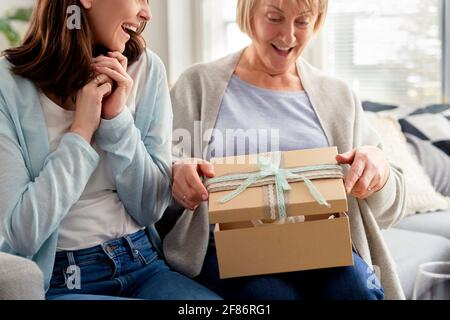 Aufgeregt Erwachsene Tochter wartet auf Mutter, um das Geschenk zu öffnen Stockfoto