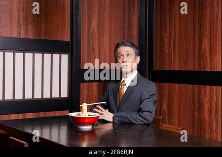 Geschäftsmann mit schwebendem Essstäbchen und Nudeln im Restaurant Stockfoto