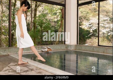 Junge Frau in einem Handtuch, die bei Onsen den Zeh in Wasser taucht Stockfoto