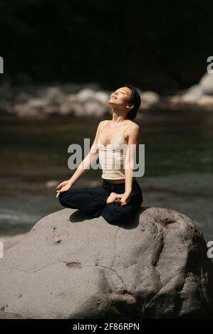 Ruhige, schöne junge Frau, die in Lotushaltung bei Sonnenschein meditiert Rock Stockfoto