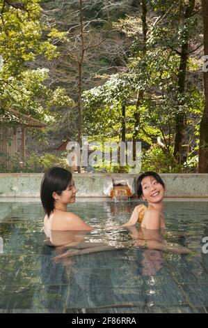 Junge Frau mit Luder, die den Rücken des Freundes im Pool schrubbt Onsen Stockfoto