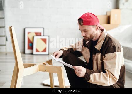 Young Möbel Assemblage Spezialist durch die Anweisung auf Papier beim Zusammenbau Holzstuhl im Studio, Haus oder Wohnung Stockfoto