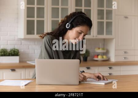 Nahaufnahme lächelnde Frau mit Kopfhörern, die Notizen macht, online studiert Stockfoto