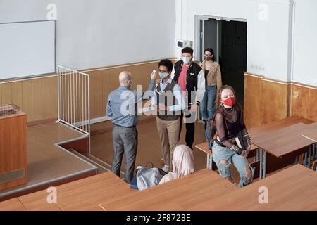 Reife kahle männliche Professor mit Thermometer Messung Körpertemperatur von Schüler in Schutzmasken vor der Vorlesung Stockfoto