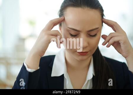 Hübsche junge Unternehmerin, die unter starken Kopfschmerzen oder Migräne leidet Nach der Arbeit den ganzen Tag Stockfoto