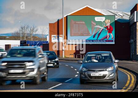 Greenock, Inverclyde, Schottland, Großbritannien. April 2021. IM BILD: Auf einer riesigen elektronischen Plakatwand zeigt Nicola Sturgeon, wie sie eine riesige Schere in einer Nachstellung der Dienstkürzungen ihrer Regierung im Royal Hospital von Inverclyde führt, nachdem sie versprochen hatte, sie zu behalten. Scotland Matters Pressemitteilung Link: https://www.scotlandmatters.co.uk/inverclyde-hospital-cuts-billboard-by-scotland-matters/ Bild: Colin Fisher/Alamy Live News Stockfoto