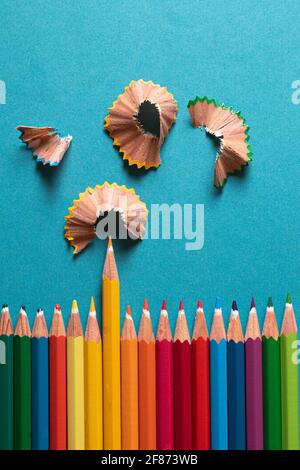 Draufsicht. Buntstifte nebeneinander mit Bleistiftabsticheln auf der Oberseite. Alles auf einem blauen Hintergrund mit einer Textur, die den gelben Bleistift hervorhebt. Stockfoto