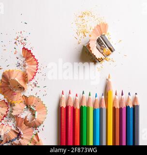 Draufsicht der Farbstifte Seite an Seite, wobei der gelbe Bleistift auf dem weißen Hintergrund hervorgehoben wird. Mit farbigen Bleistiftabfällen auf der linken Seite und einem pe Stockfoto