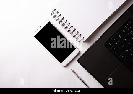 Draufsicht auf einen offenen Laptop mit Stift, Handy und Ringnotizbuch. Stockfoto