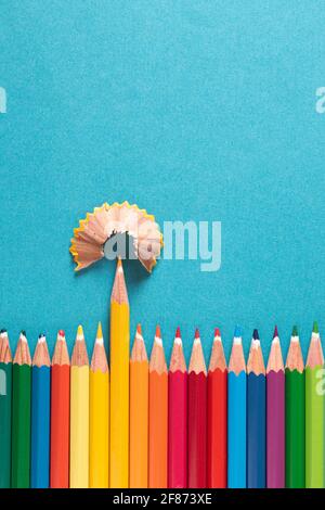 Draufsicht. Buntstifte nebeneinander mit einer Bleistiftrasur auf der Oberseite. Alles auf einem blauen Hintergrund mit einer Textur, die den gelben Bleistift hervorhebt. Stockfoto