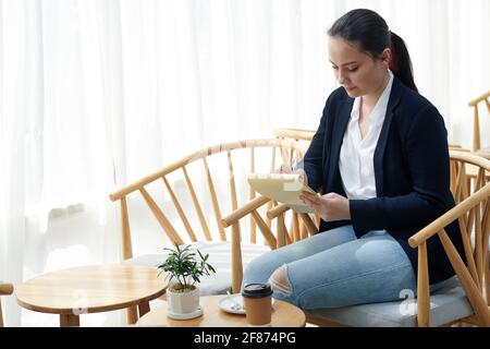 Junge Frau verbringt den Morgen im Coffeeshop, trinkt Kaffee und schreibt Gedanken und Ideen über die Geschäftsentwicklung in Notizbüchern Stockfoto
