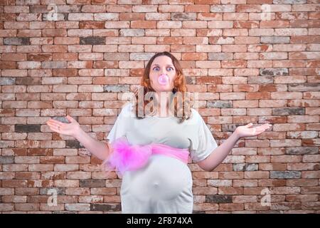 Eine Schwangere mit einem Bogen und einer Blase aufgeblasen Mit Gummi auf dem Hintergrund einer roten Ziegelwand Stockfoto