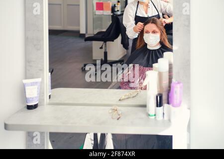 Eine Frau bekommt in einem Friseurladen die Haare geschnitten In einer medizinischen Gesichtsmaske Stockfoto