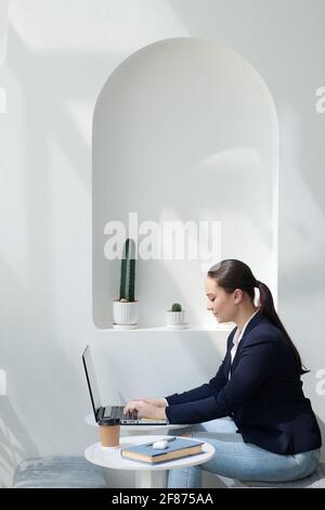 Lächelnde junge Unternehmerin, die in einem modernen Café am Tisch sitzt Und die Beantwortung von E-Mails auf dem Laptop Stockfoto