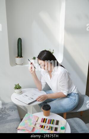 Talentierte kreative junge Frau, die mit Bleistift porträtiert und trinkt Kaffee Stockfoto