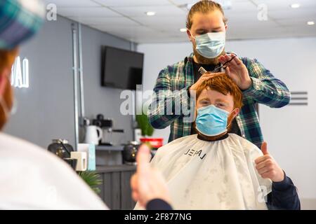 Halesowen, West Midlands, Großbritannien. April 2021. Firmenchef Rhys Barrett, 27, gibt die Daumen nach oben, als er seine Haare von Sam Whitlock, Miteigentümer von Label Male Image in Halesowen, West Midlands, schneiden lässt. Nach der Lockerung der Covid-Beschränkungen heute öffnen sich die Barbiere. Kredit: Peter Lopeman/Alamy Live Nachrichten Stockfoto