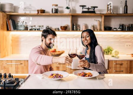 Nettes multiethnisches Paar, das zusammen in der Küche zu Mittag gegessen und ein Glas Wein getrunken hat. Stockfoto
