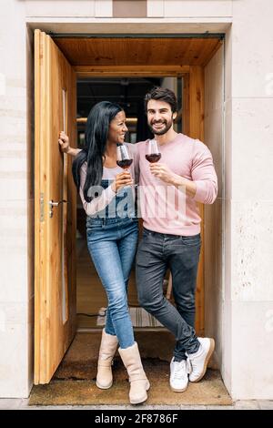 Nettes multiethnisches Paar, das zu Hause ein Glas Wein trinkt und die Kamera anschaut. Stockfoto