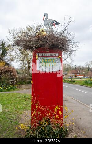 Rote Telefonbox, die zu Ostern mit einem künstlichen Störche-Nest auf der Oberseite dekoriert ist, Compton Village, Surrey, England, Großbritannien Stockfoto