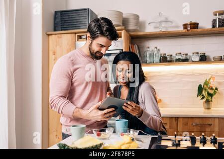 Glückliches Paar, das zu Hause in der Küche frühstücken und ein Tablet benutzen kann. Stockfoto