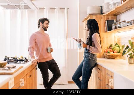 Schöne schwarze Frau und ihr Freund telefonieren, während sie zu Hause in der Küche stehen. Stockfoto