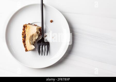 Bissen Sie ein Stück veganen Tofu-Käsekuchen auf eine weiße Untertasse. Gesundes Dessertkonzept auf pflanzlicher Basis. Stockfoto