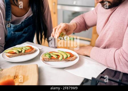 Unbekannter Mann, der in der Küche neben ihrer Freundin sitzt und ein leckeres Frühstück zubereitet. Stockfoto