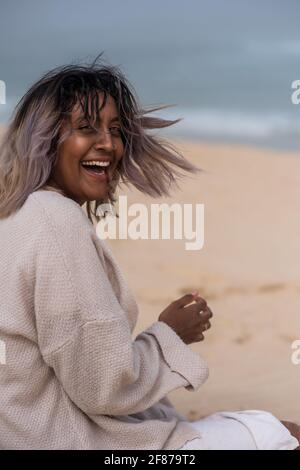 Porträt einer glücklichen Frau, die am Strand auf Sand sitzt Stockfoto