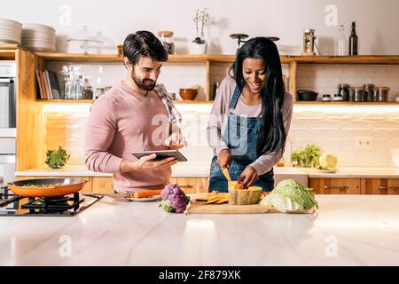 Nettes Paar bereitet das Mittagessen zusammen in der Küche zu Hause und mit Tablet. Stockfoto