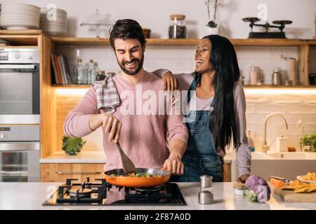 Nettes Paar lächelt und bereitet das Mittagessen zusammen in der Küche zu Hause. Stockfoto