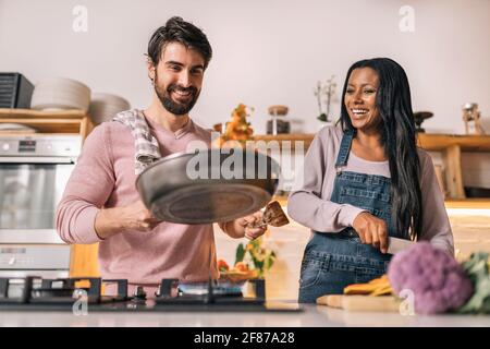 Nettes Paar lächelt und bereitet das Mittagessen zusammen in der Küche zu Hause. Stockfoto