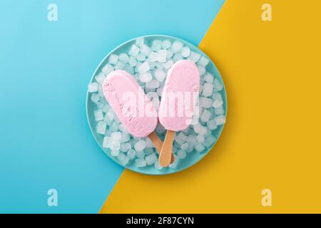 Erdbeerpopsicles und zerkleinertes Eis auf blauem Teller und gelb Und blauer Hintergrund Stockfoto