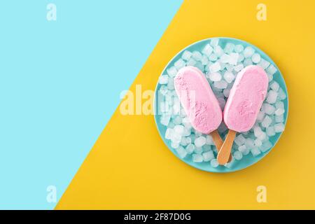 Erdbeerpopsicles und zerkleinertes Eis auf blauem Teller und gelb Und blauer Hintergrund Stockfoto