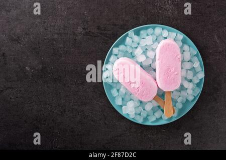 Erdbeerpopsicles und zerkleinertes Eis auf schwarzem Schiefer-Hintergrund Stockfoto