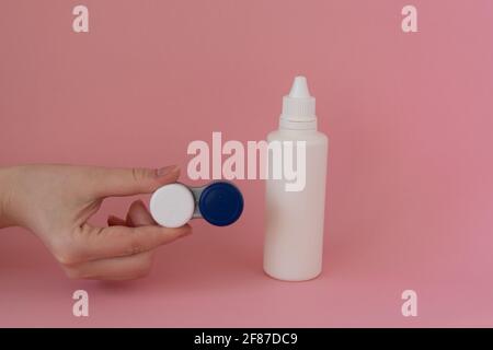 Kontaktlinsengehäuse in der Hand einer Frau und Flasche Lösung auf rosa Hintergrund Stockfoto