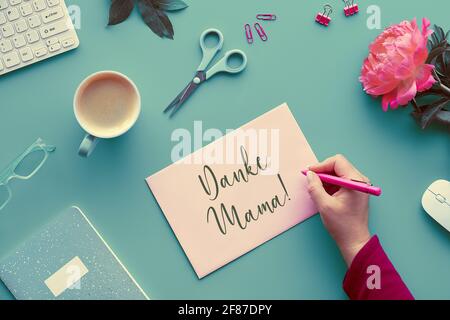 Grußkarte zum Muttertag. Text Danke Mama bedeutet Danke Mama auf Deutsch. Pinke Pfingstrosen auf verblassten mintgrünen Tischen. Kaffee, Tastatur, Blumen Stockfoto