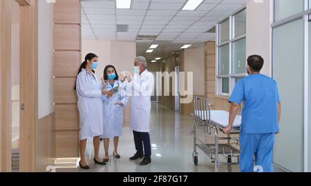 Leitende professionelle Arzt konsultieren und diskutieren mit Frau Ärzte in Schwere Tumor-und Krebs-Operation Fall, während männliche Krankenschwester schieben Trage-Liege b Stockfoto