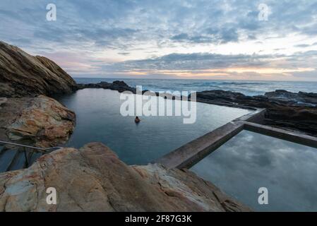 Zwei (verschwommene) Personen umarmen sich im berühmten Blue Pool (Denkmalgeschütztes Meerwasser-Schwimmbad) In Bermagui an der Südküste von New South Wales Australien in der Abenddämmerung Stockfoto