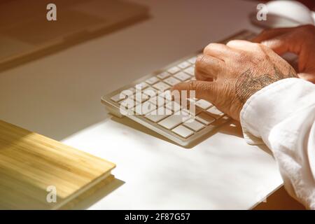 Hände eines tätowierten Mannes auf der Tastatur eines Notebook Stockfoto