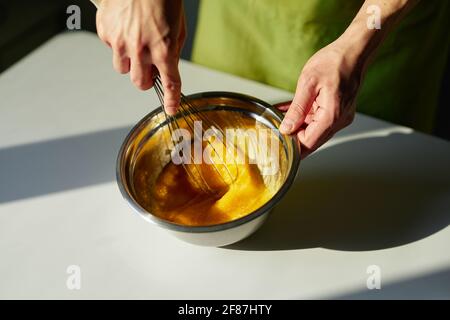 Leckere hausgemachte Kuchen backen, Oster-Kuchen Vorbereitung oder Cookie-Konzept. Koch in grüner Schürze, der Zucker und Eier in einer Edelstahlschüssel mit Drahtbesen mischt. Hochwertige Fotos Stockfoto