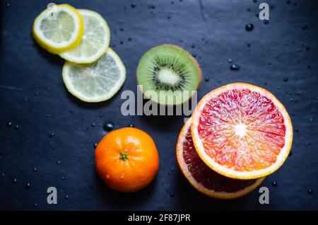 Mischen Sie frische tropische Früchte wie Blutorange, Clementine und Zitronenscheiben auf der Rückseite der Arbeitsplatte, die mit Wassertropfen bedeckt ist. Stockfoto