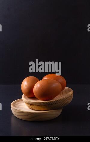Drei Hühnereier auf zwei Holztellern mit schwarzem Hintergrund Stockfoto